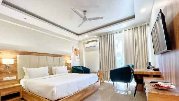 A modern hotel room with a large bed, a desk, a chair, a television, and a ceiling fan. - Hotel Golf View Suites (Gurugram)