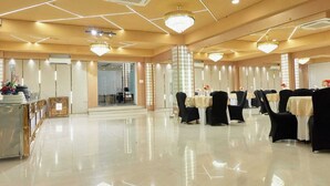 A spacious banquet hall with a polished floor, multiple tables set for dining, and elegant chandeliers. - Hotel Golf View Suites (Gurugram)