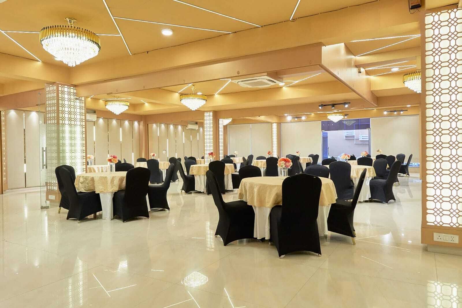 Uma sala de banquetes com mesas redondas, cadeiras pretas e lustres.