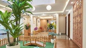 A hotel lobby with a wooden reception desk, a small bridge, and potted plants. - Hotel Golf View Suites (Gurugram)