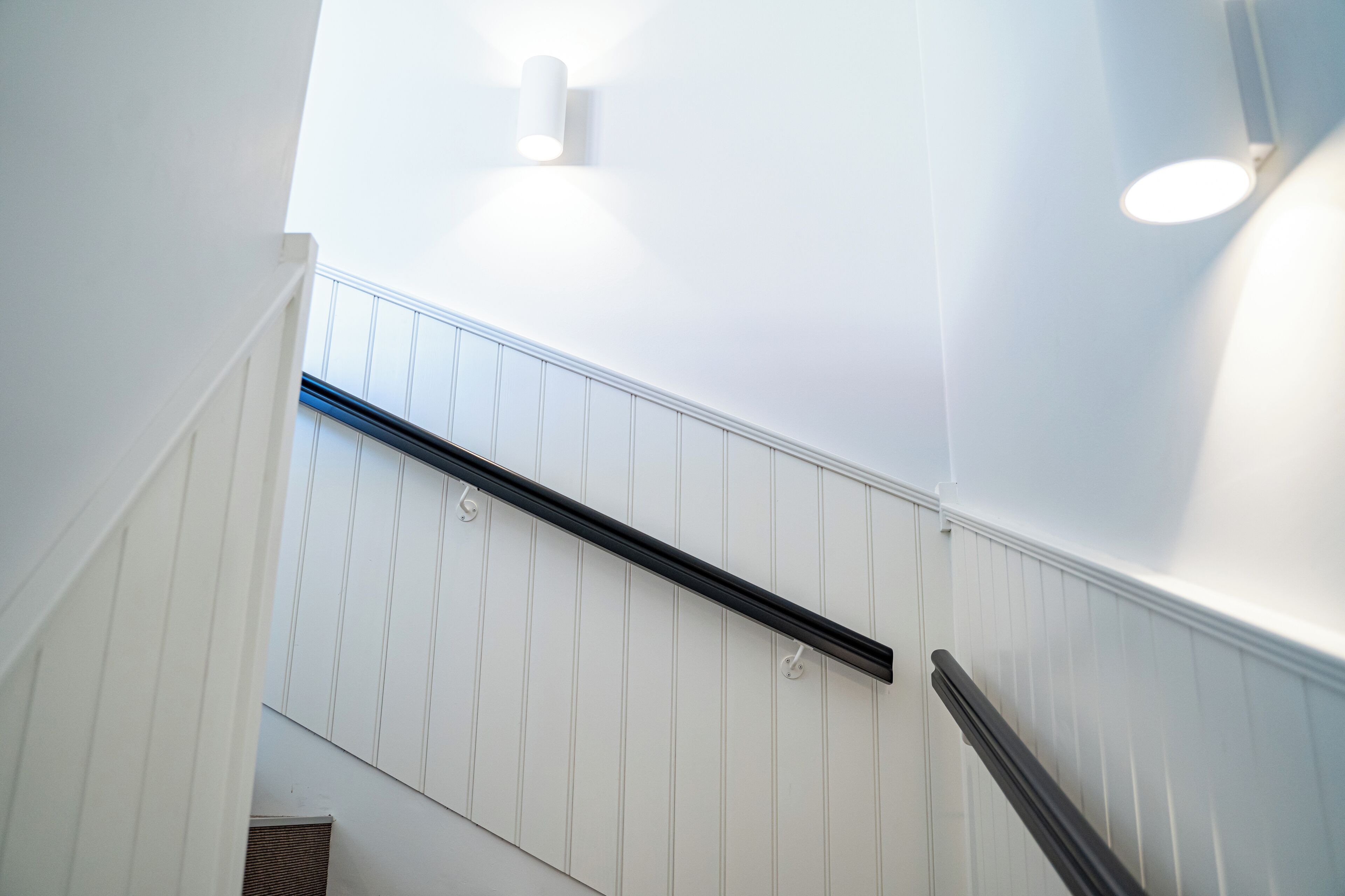 A staircase with white paneling and black handrails.