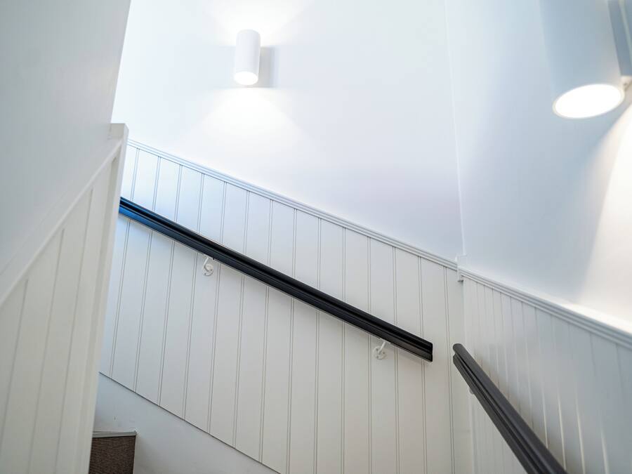 A staircase with white paneling and black handrails.
