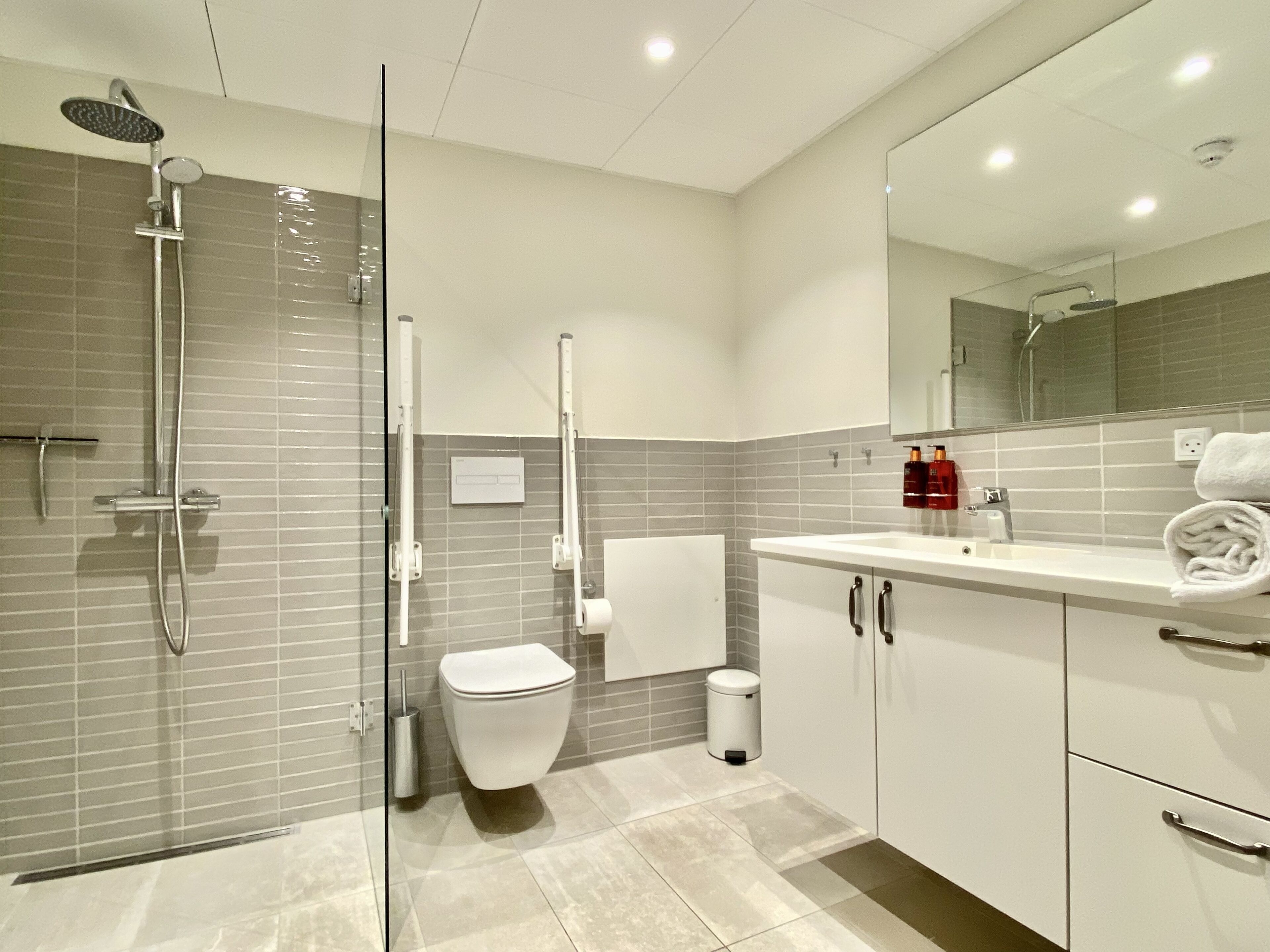 Un baño moderno con cabina de ducha de vidrio, inodoro, lavabo con espejo y un cubo de basura.