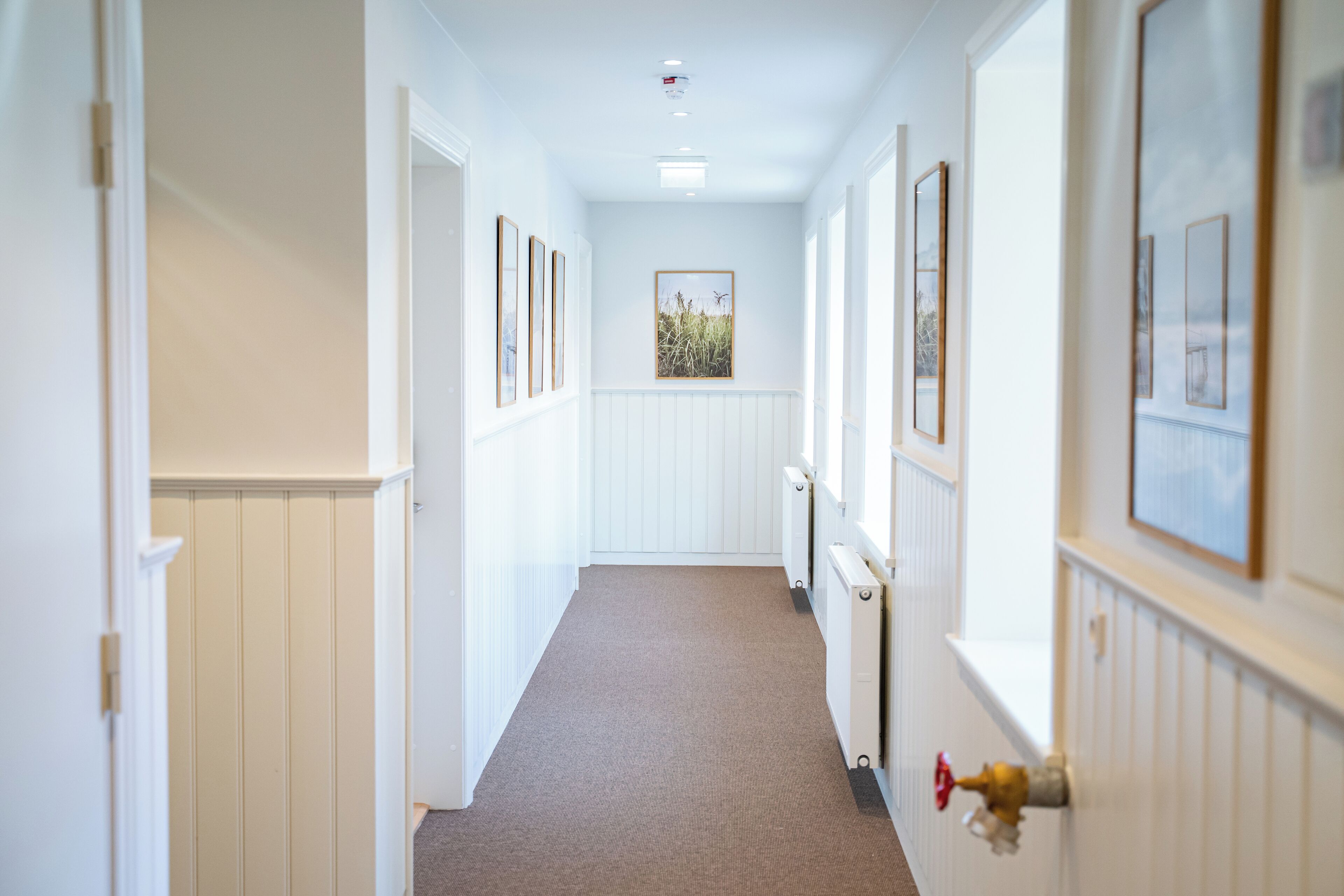 A hallway with white walls, framed pictures, and a radiator.