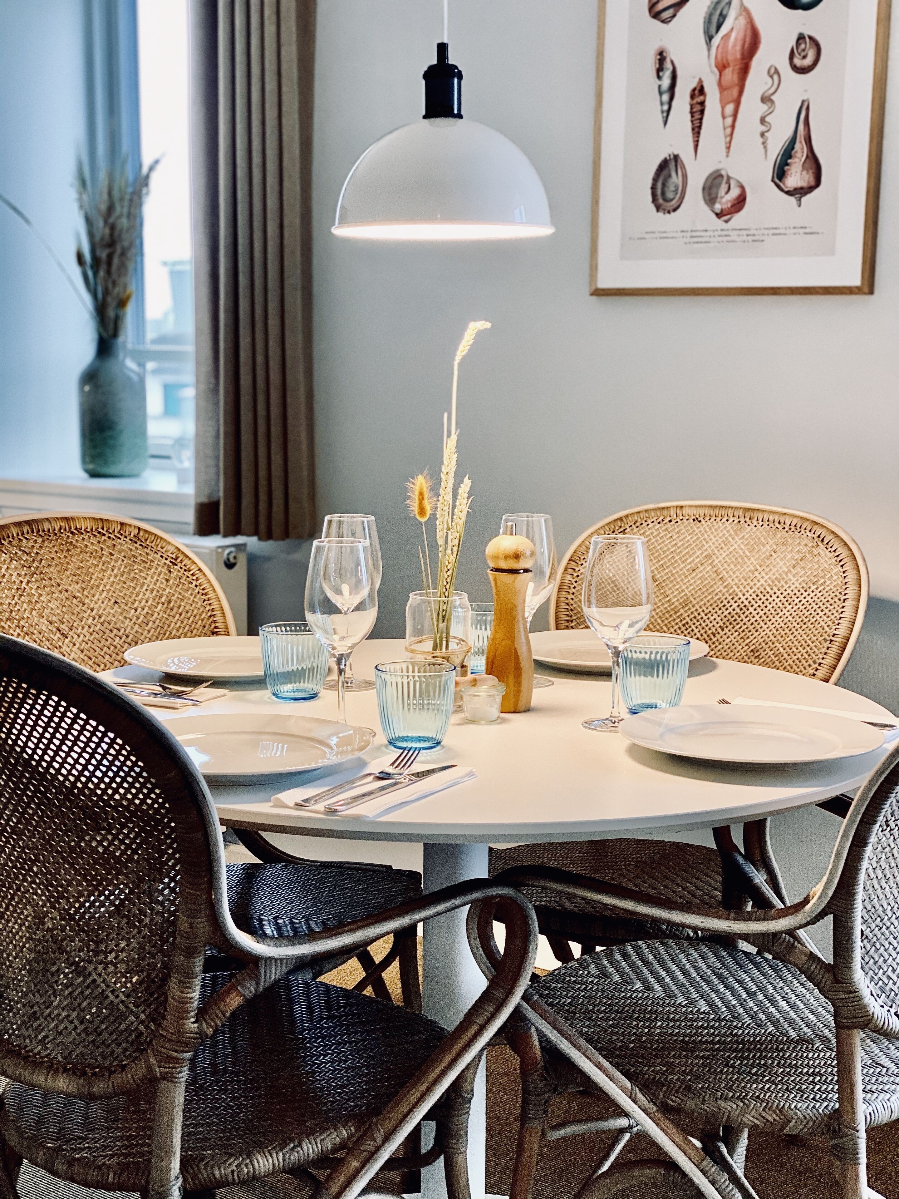 A round dining table with a white tablecloth, surrounded by wicker chairs.