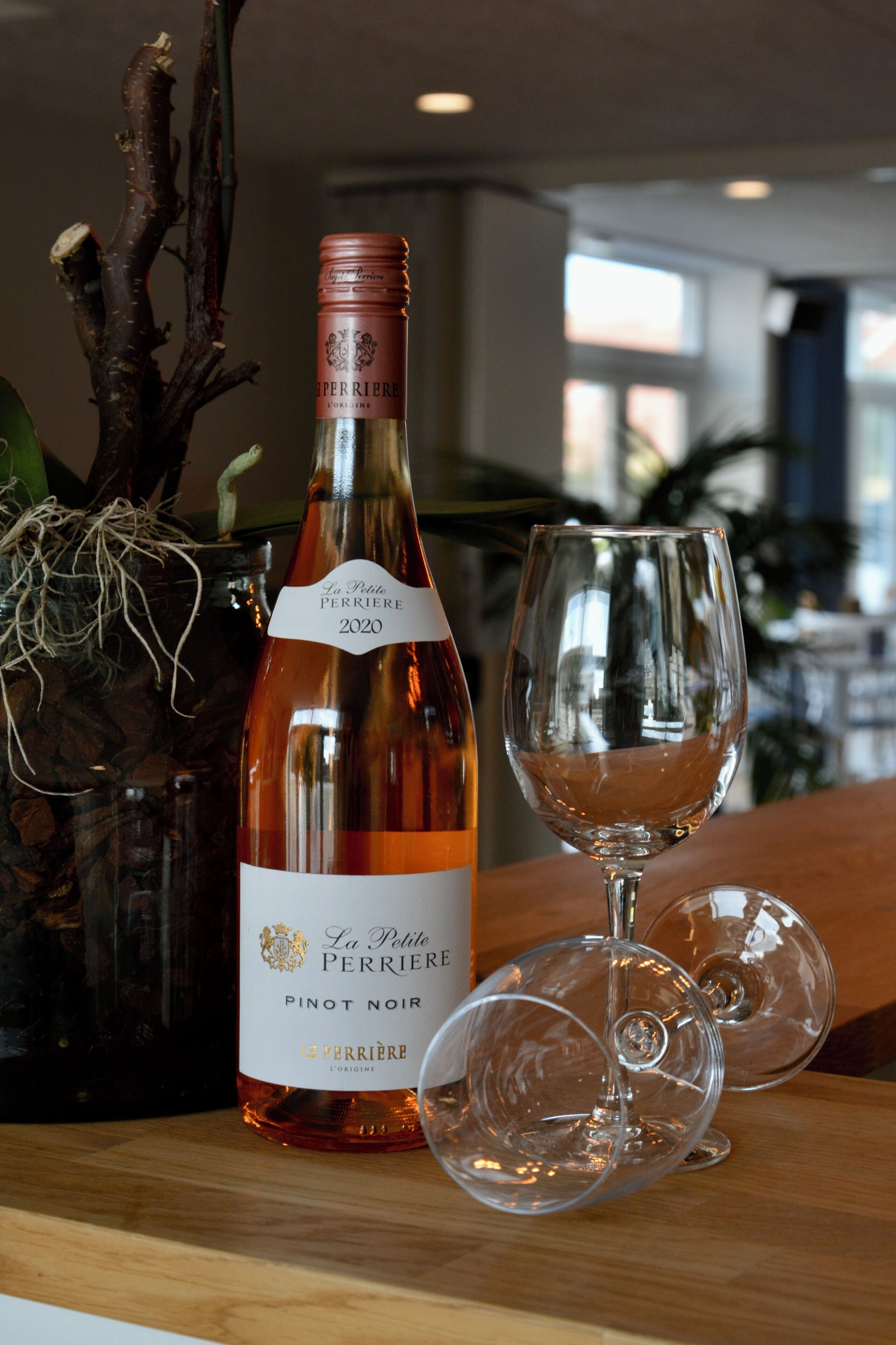 A bottle of La Petite Perriere Pinot Noir wine and two empty wine glasses on a wooden surface.