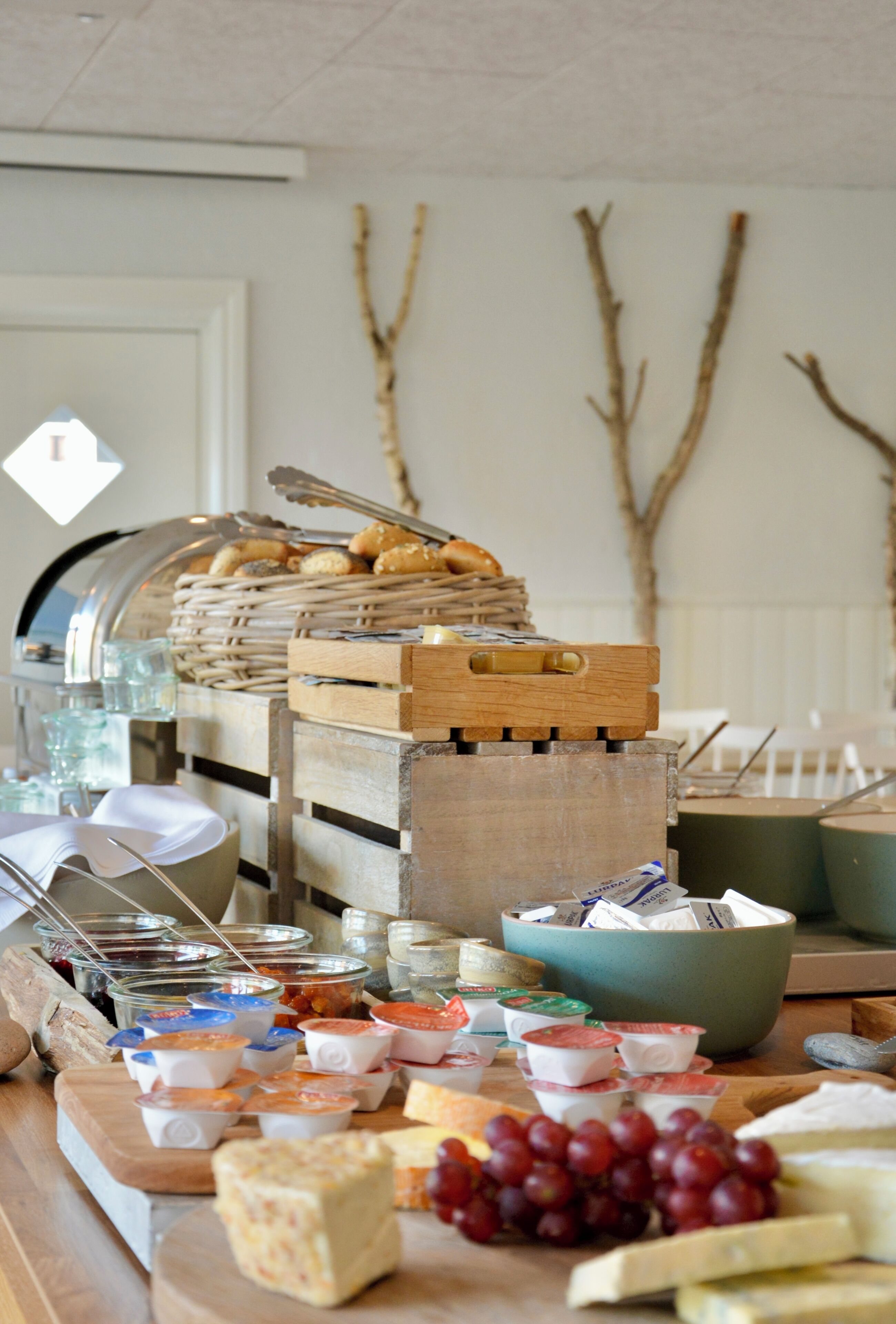 A buffet table with various food items, including cheese, grapes, and condiments.
