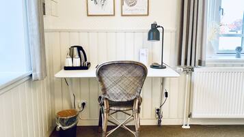 A room with a white desk, a wicker chair, a coffee maker, a framed butterfly picture, and a radiator.