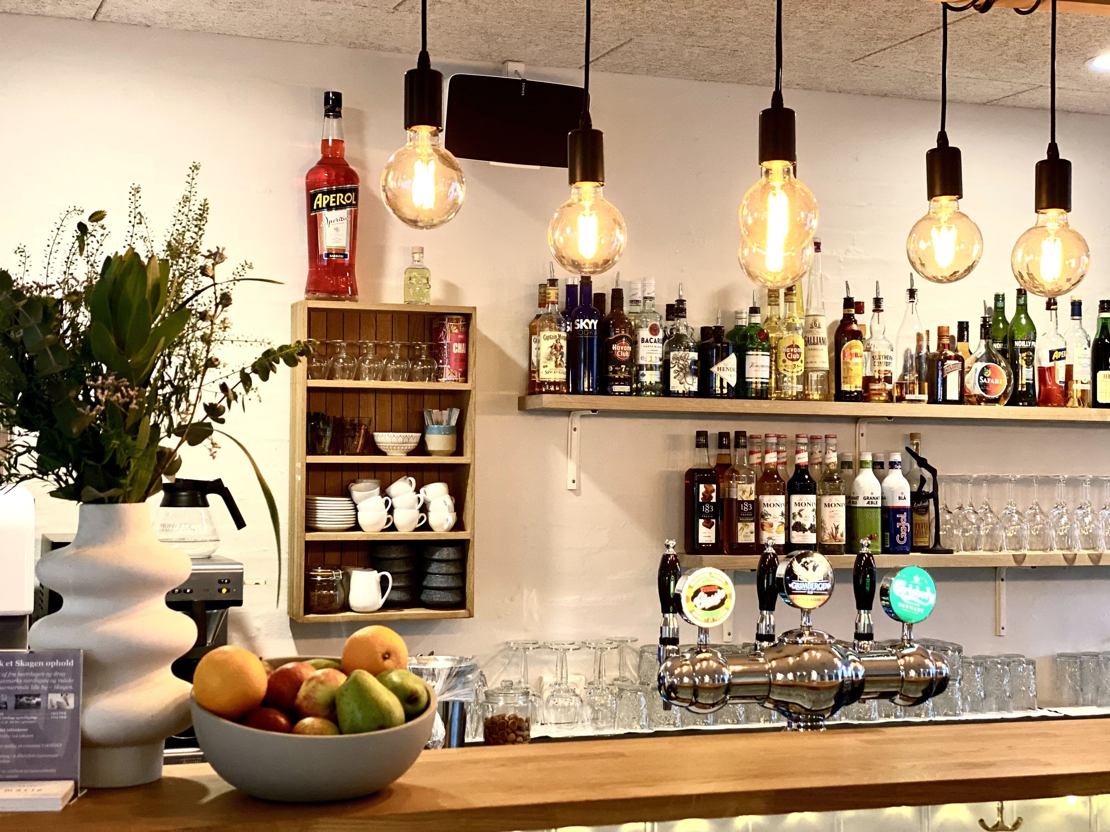 A bar area with a variety of liquor bottles, a fruit bowl, and a beer tap.