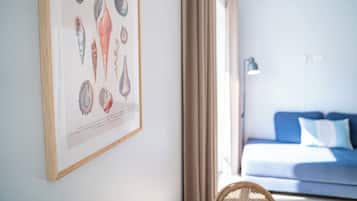 Una ilustración enmarcda de vida marina en una pared, una cama con cabecera azul y una ventana con cortinas.