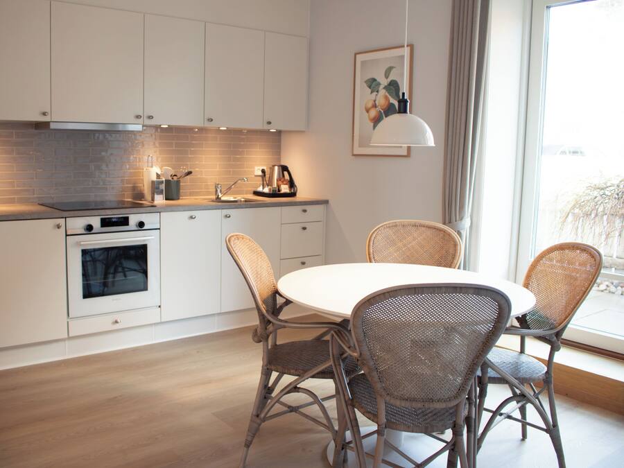 Una cocina moderna con armarios blancos, horno empotrado, una mesa de comedor con sillas de mimbre y un ventanal con vistas.
