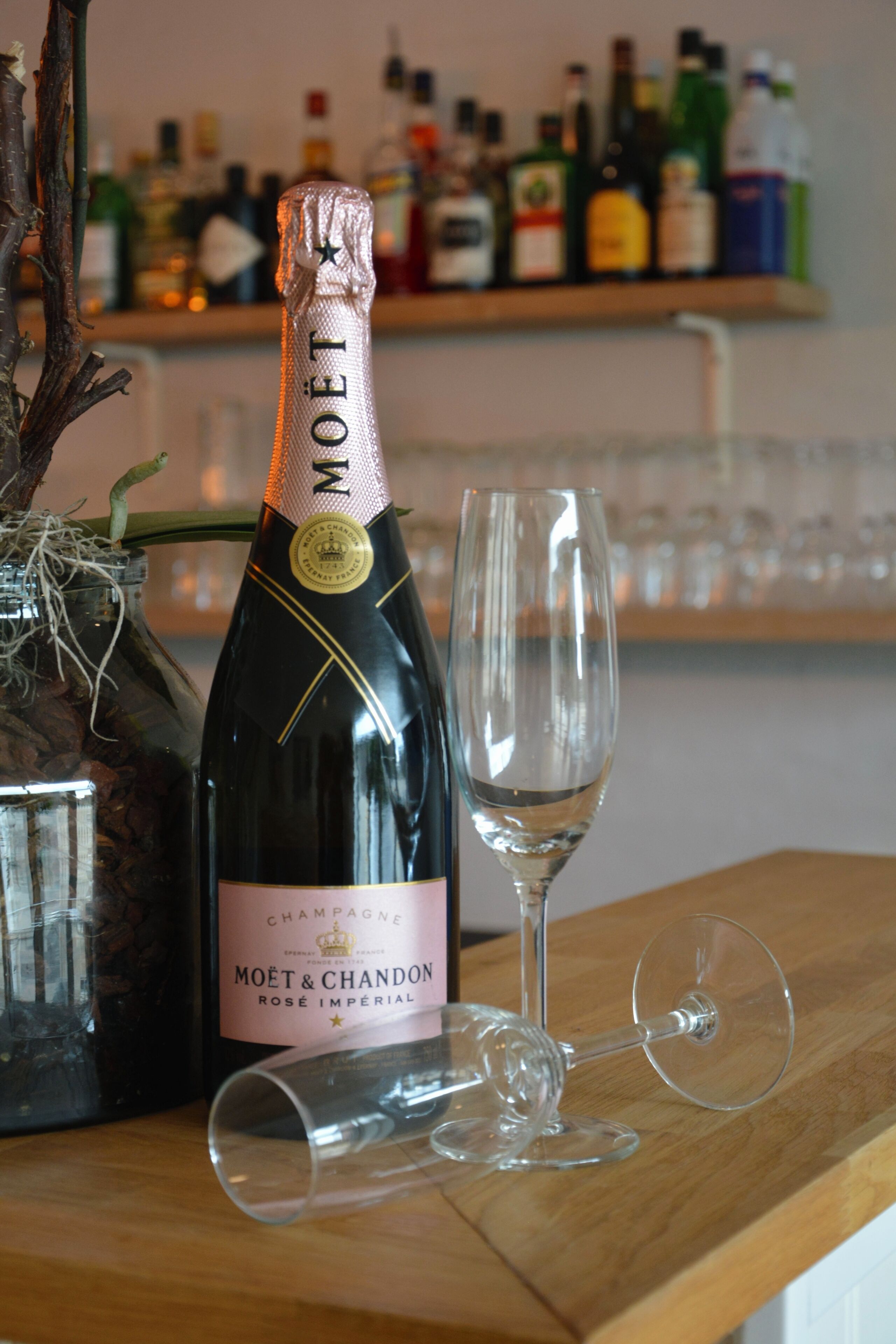 Una botella de Moët & Chandon Rosé & Imperial champagne y una copa de vino sobre una superficie de madera.