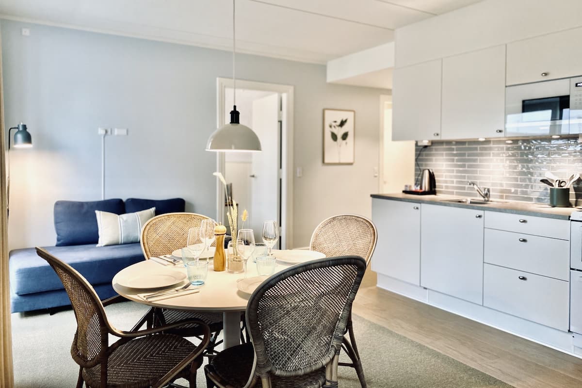 Una cocina moderna con armarios blancos, un comedor con sillas de mimbre y un sofá azul.