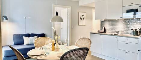 A modern kitchen with white cabinets, a dining area with wicker chairs, and a blue sofa.
