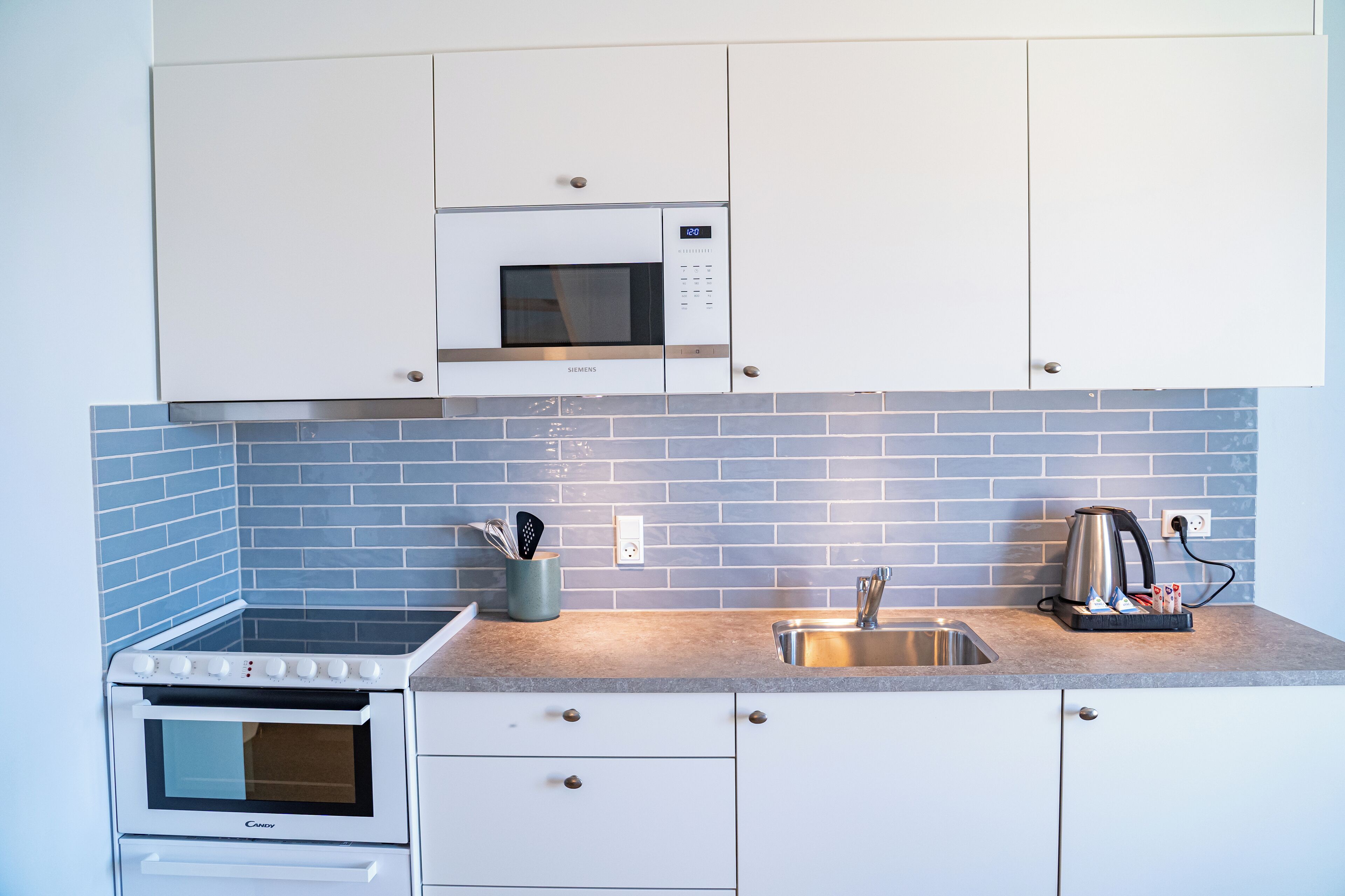 A modern kitchen with white cabinets, a built-in microwave, a stove, and a sink.