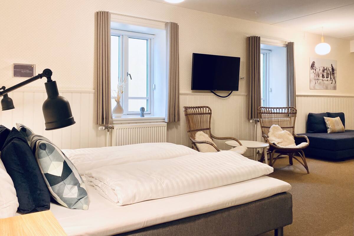 Habitación de hotel con cama, escritorio, dos sillas, televisión y ventana con cortinas.