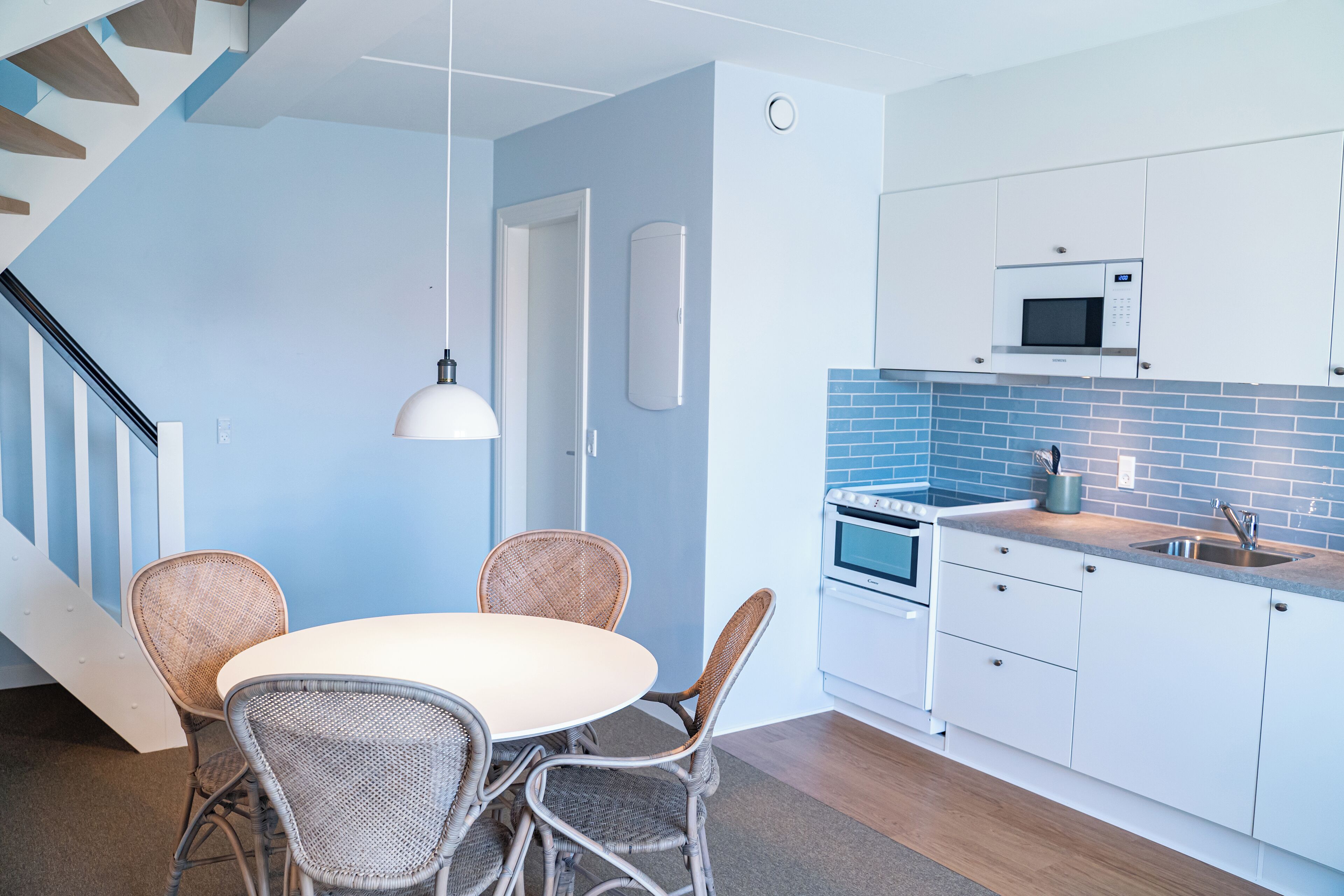 Una cocina moderna con armarios blancos, un salpicadero azul y una mesa de comedor blanca con sillas de mimbre.