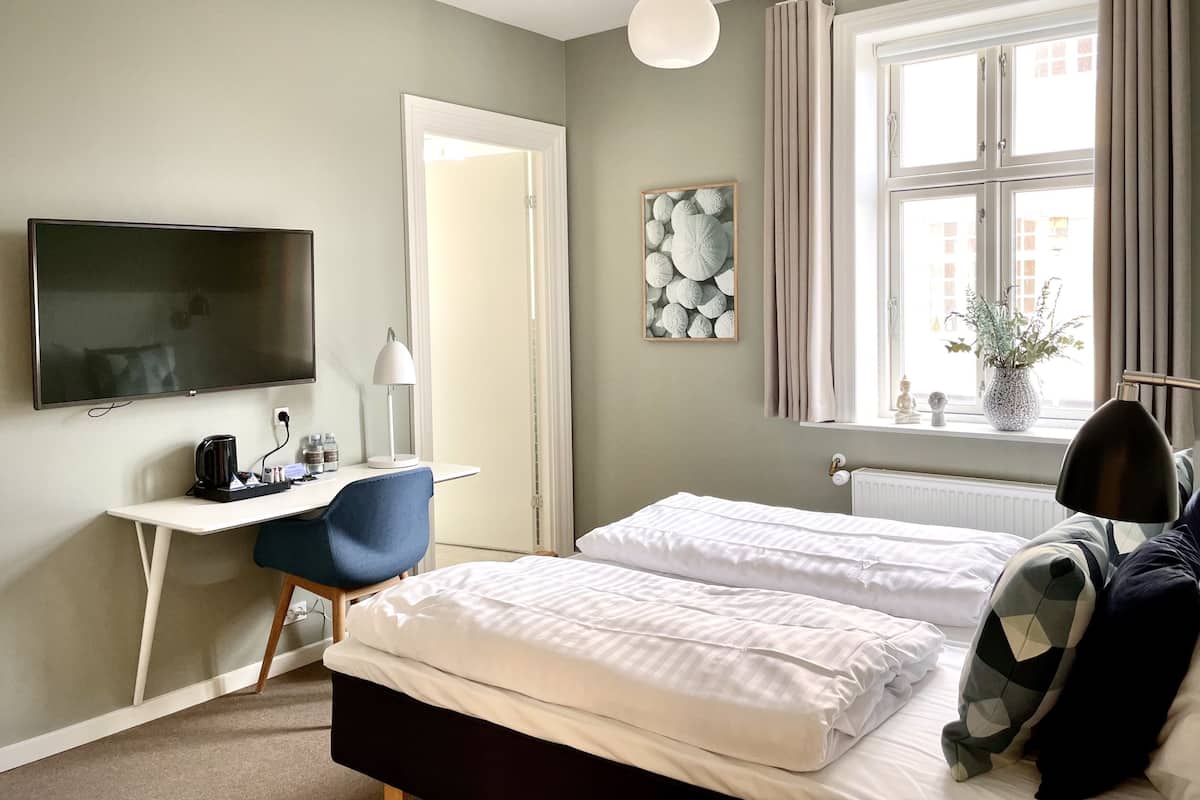 Habitación de hotel con cama, escritorio con silla, televisor y ventana con cortinas.