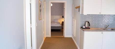 A compact hotel room with a kitchenette, a bed, and a hallway leading to a bathroom.