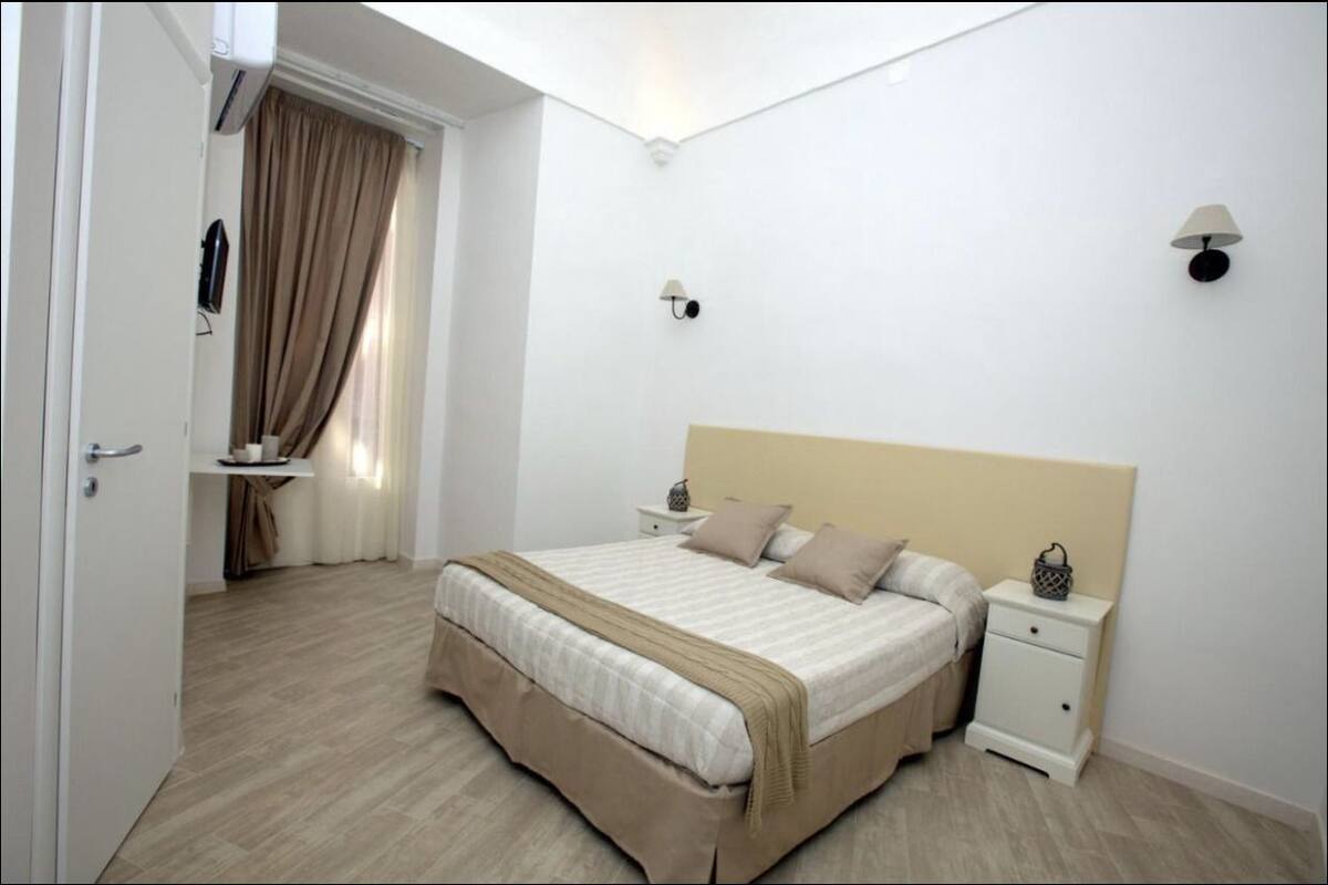 Une chambre à coucher avec un lit, des tables de chevet, une lampe et une fenêtre avec des rideaux.