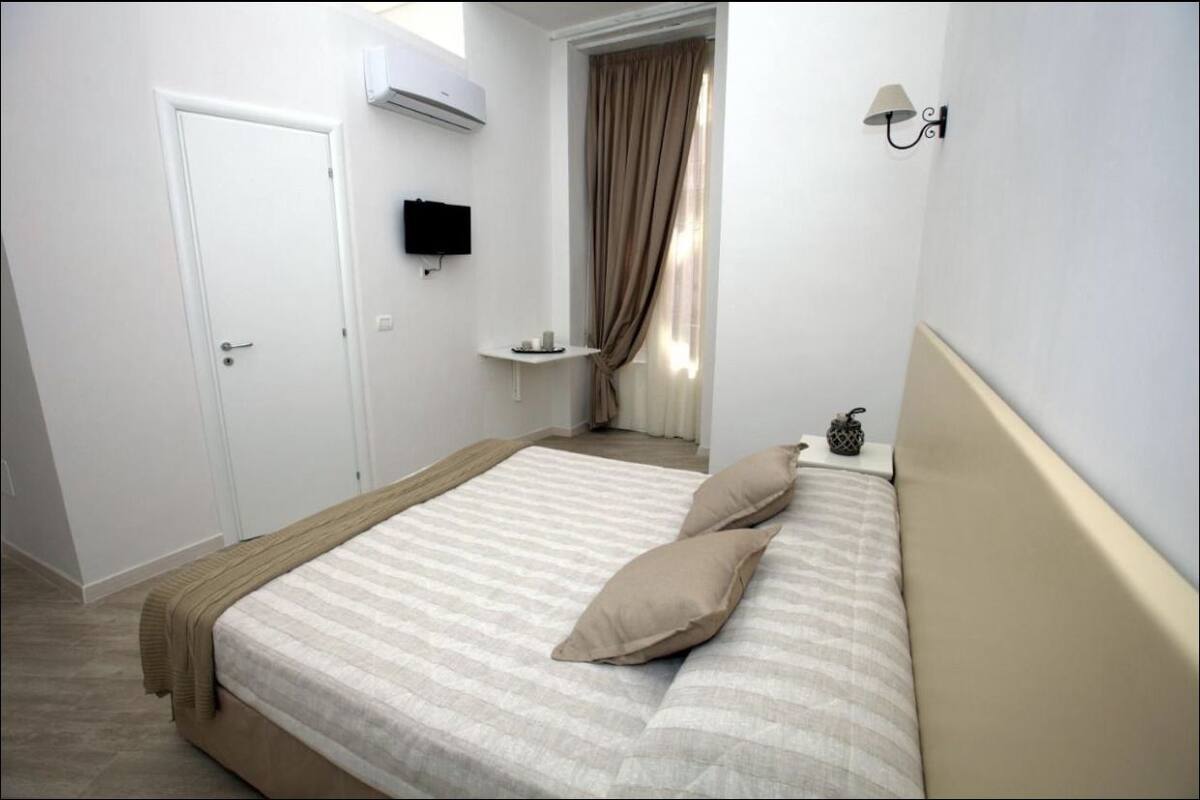 Une chambre à coucher avec un lit, une table de chevet, un téléviseur fixé au mur et une porte.