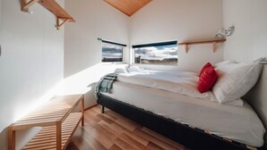 A bedroom with a bed, wooden bench, and two windows with a view. - Blue View Cabin 6A with Hot Tub (Bláskógabyggd)