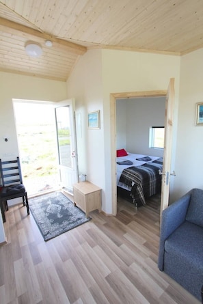 A room with a wooden ceiling, a bed with a red pillow, a small table, and a chair. - Blue View Cabin 1B with Hot Tub (Bláskógabyggd)