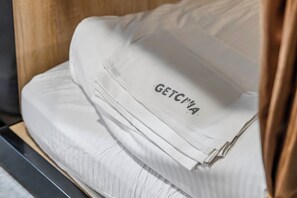 Un lit bien fait, avec une couette blanche et un oreiller orné du mot « GETCYA ».