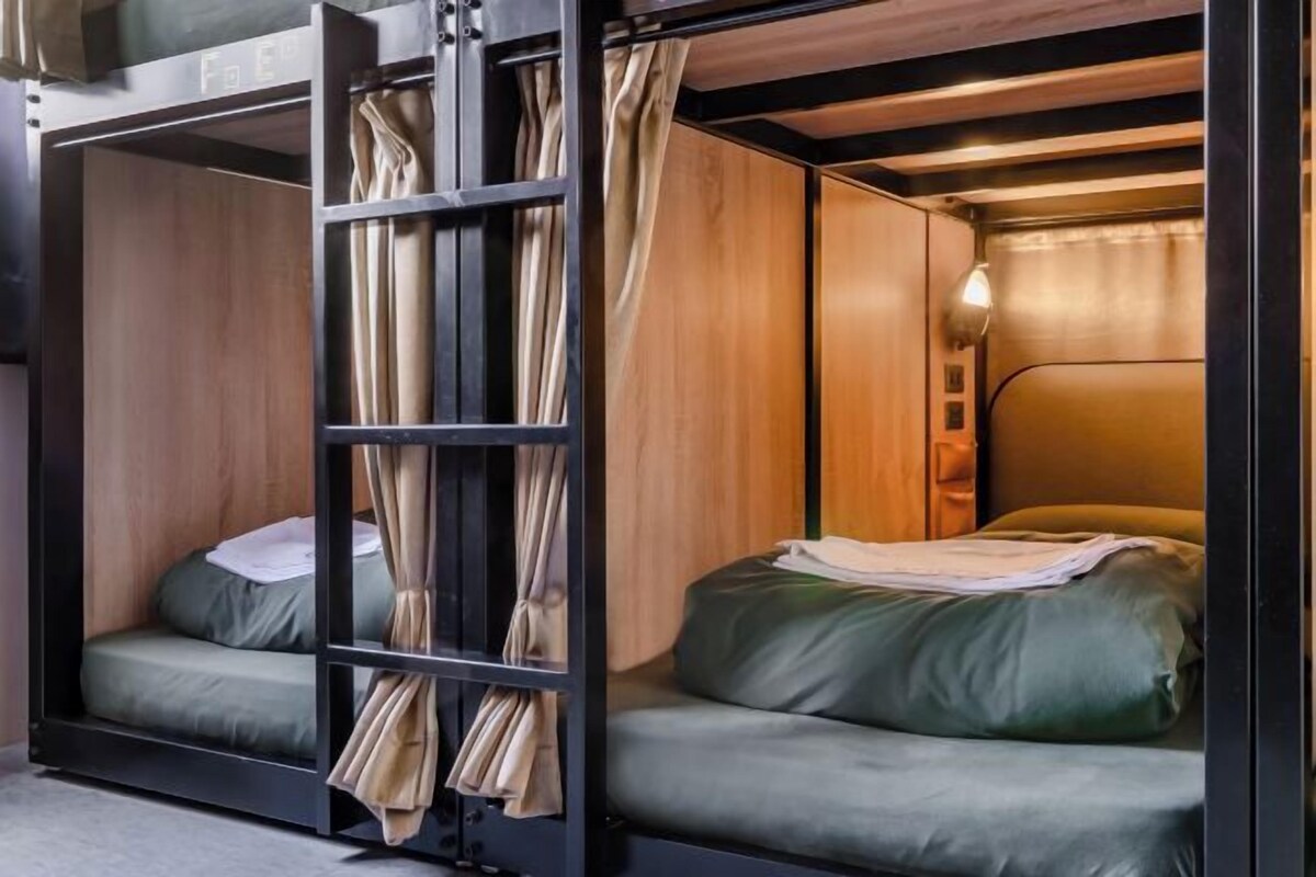 A compact, modern room with a bunk bed and a single bed, wooden walls, and a built-in shelf with curtains.
