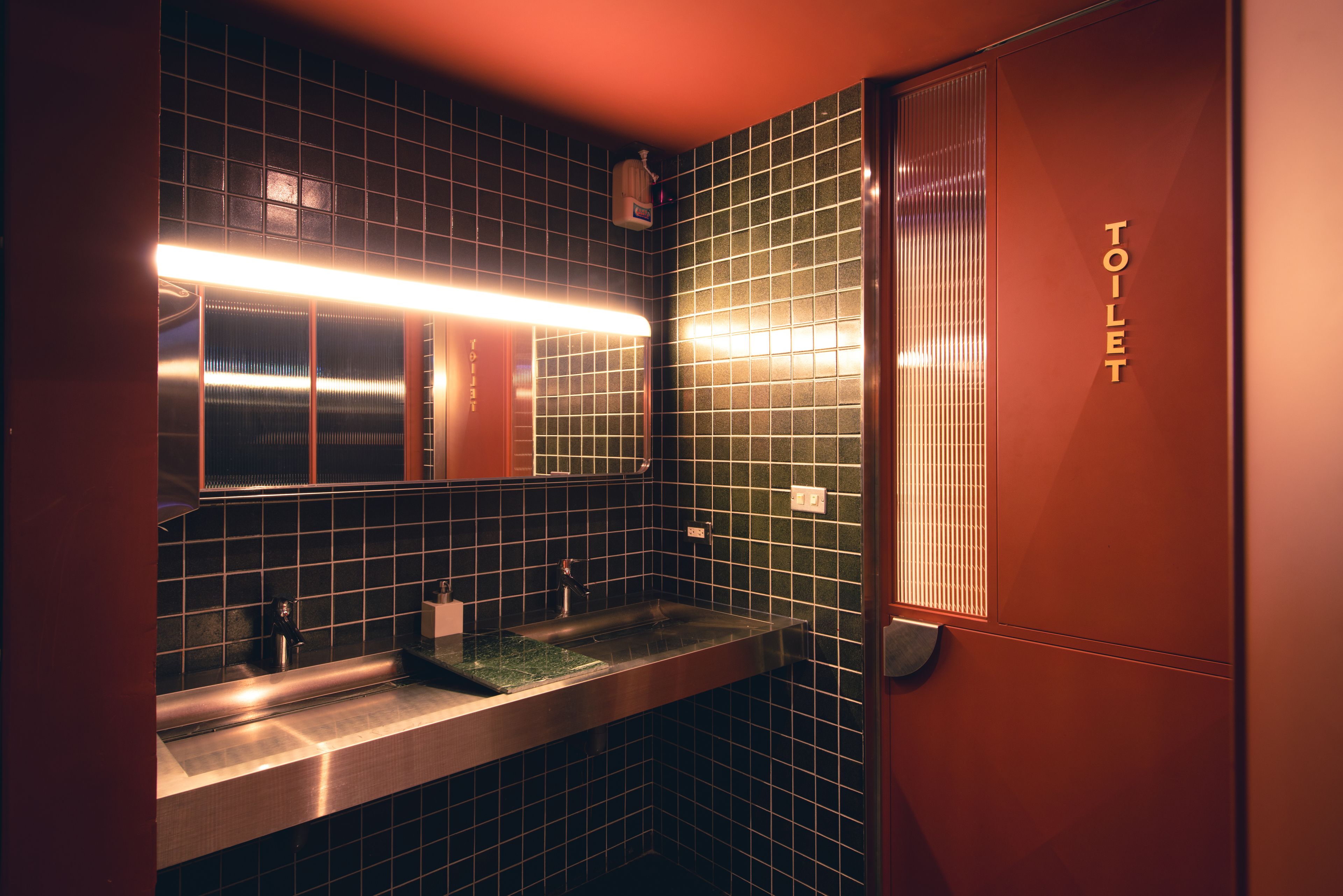 A restroom with a tiled wall, a sink, a mirror, and a toilet.