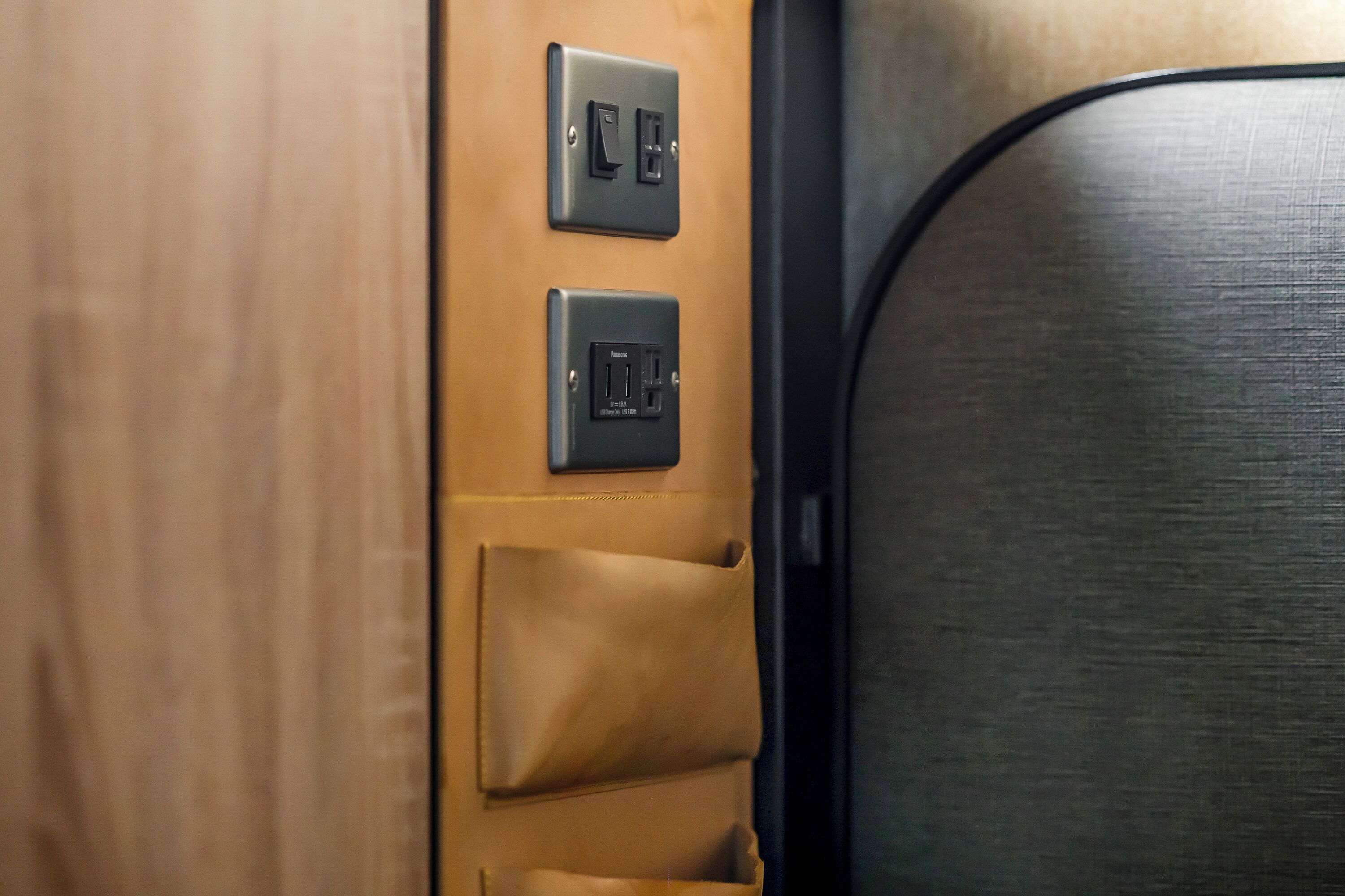 A wooden panel with two electrical outlets and a brown leather-like material.