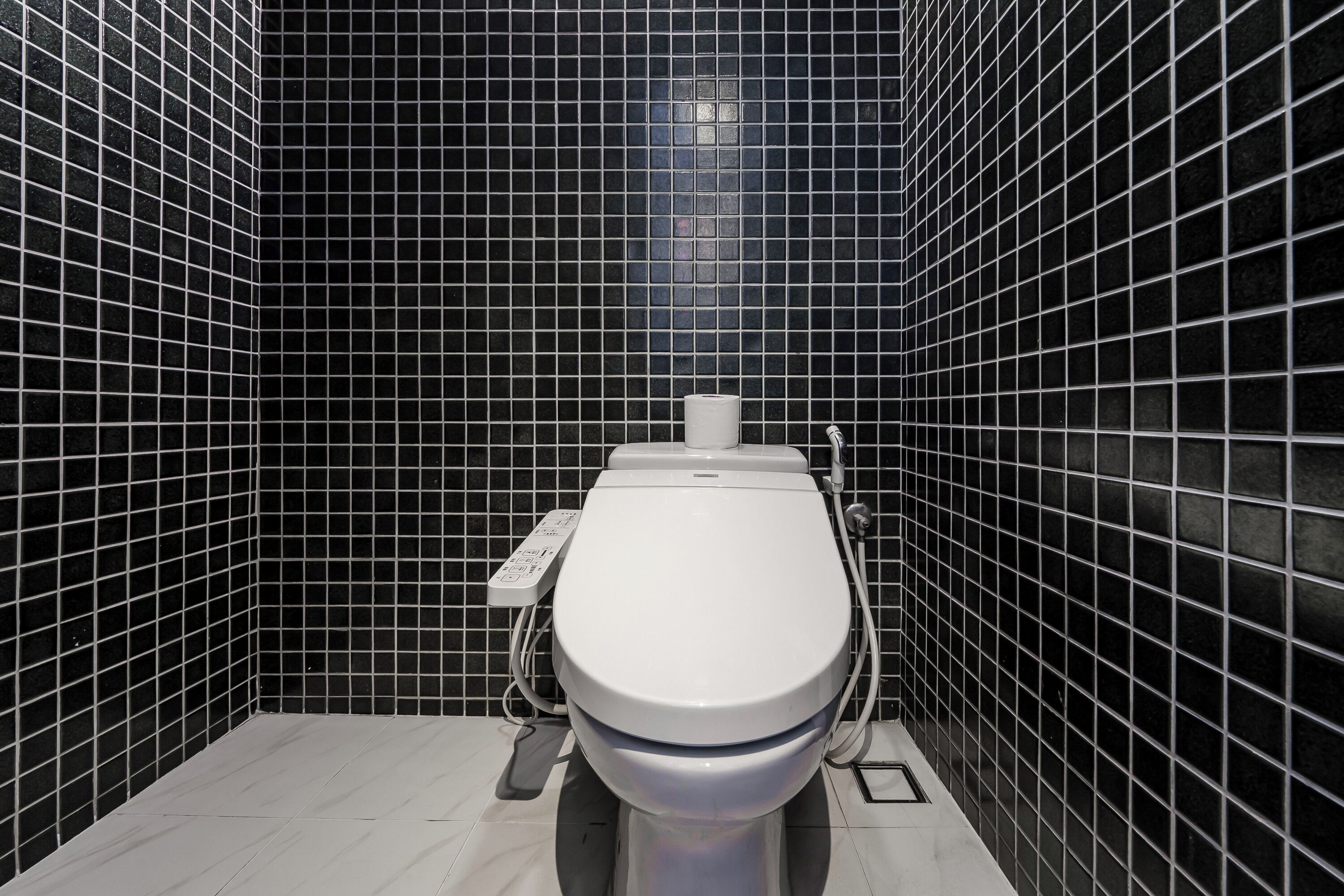 Un baño moderno con inodoro, paredes de azulejos negros y suelo blanco.