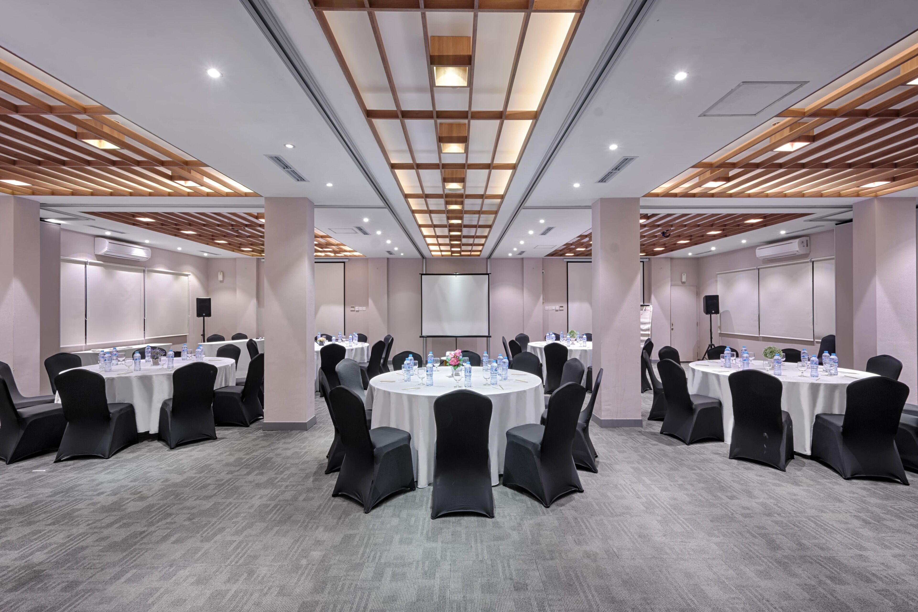 A conference room with round tables, black chairs, and a projector screen.
