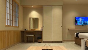 A hotel room with a wooden desk, a chair, a wardrobe, a television, and a bedside table with a heater. - Kuretakeso Kemang Hotel (Jakarta)