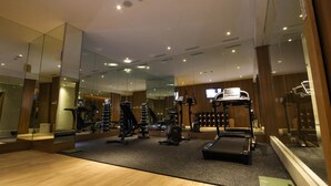 A modern gym with mirrored walls, various exercise equipment, and a television screen. - Kuretakeso Kemang Hotel (Jakarta)