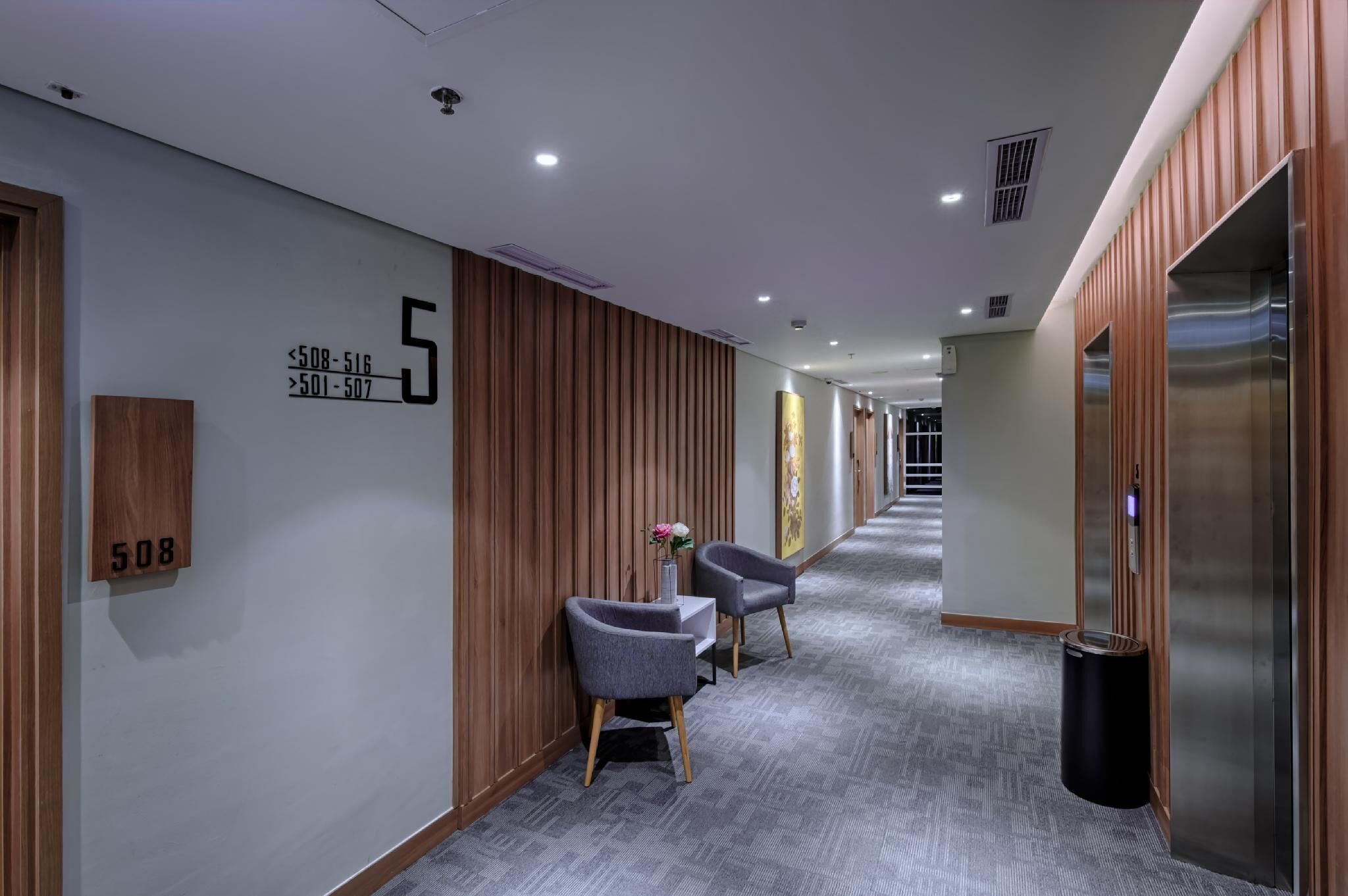A modern hotel corridor with a wooden panel wall, a number sign indicating room 508, and a trash can.