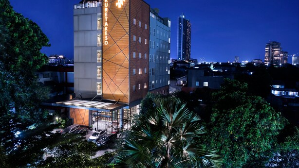 A modern hotel with a prominent 'Kuretakeso' sign, surrounded by lush greenery and other buildings in the background. - Kuretakeso Kemang Hotel (Jakarta)