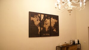 A room with a wooden dining table, a brown chair, a black console table with a coffee maker, and a world map on the wall. - B&B Garibaldi (Pisa)