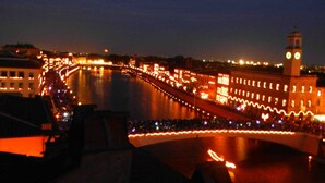 A nighttime view of a bridge with illuminated lights and a clock tower in the background. - B&B Garibaldi (Pisa)