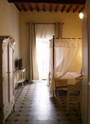 A bedroom with a four-poster bed, a bedside table, a wardrobe, and a television on a stand. - B&B Garibaldi (Pisa)