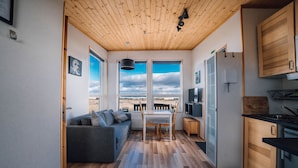 Une cuisine de taille réduite avec des meubles en bois, un coin repas comprenant une table et des chaises, et un canapé gris.
