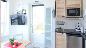 Une cuisine compacte équipée d’un four à micro-ondes, d’un réfrigérateur et d’un évier. On y trouve une table à manger avec des chaises et une petite plante.