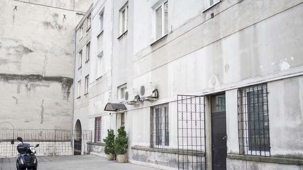 A narrow urban street with a parked scooter, a building with multiple windows and air conditioning units, and a small potted plant. - AP-Apartments Górnośląska No. 24 (Warsaw)