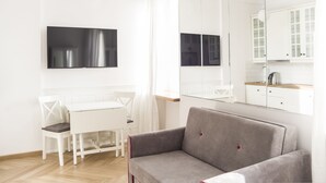 A modern, minimalist living room with a white dining table, a grey sofa, and a large mirror reflecting the kitchen area. - AP-Apartments Górnośląska No. 24 (Warsaw)