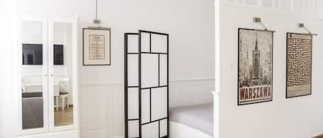 Una habitación con una cama, un armario blanco, un separador negro y dos cuadros en la pared.