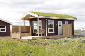 Une petite cabane en bois avec un toit recouvert d’herbe, une véranda avec un banc et une clôture en bois.