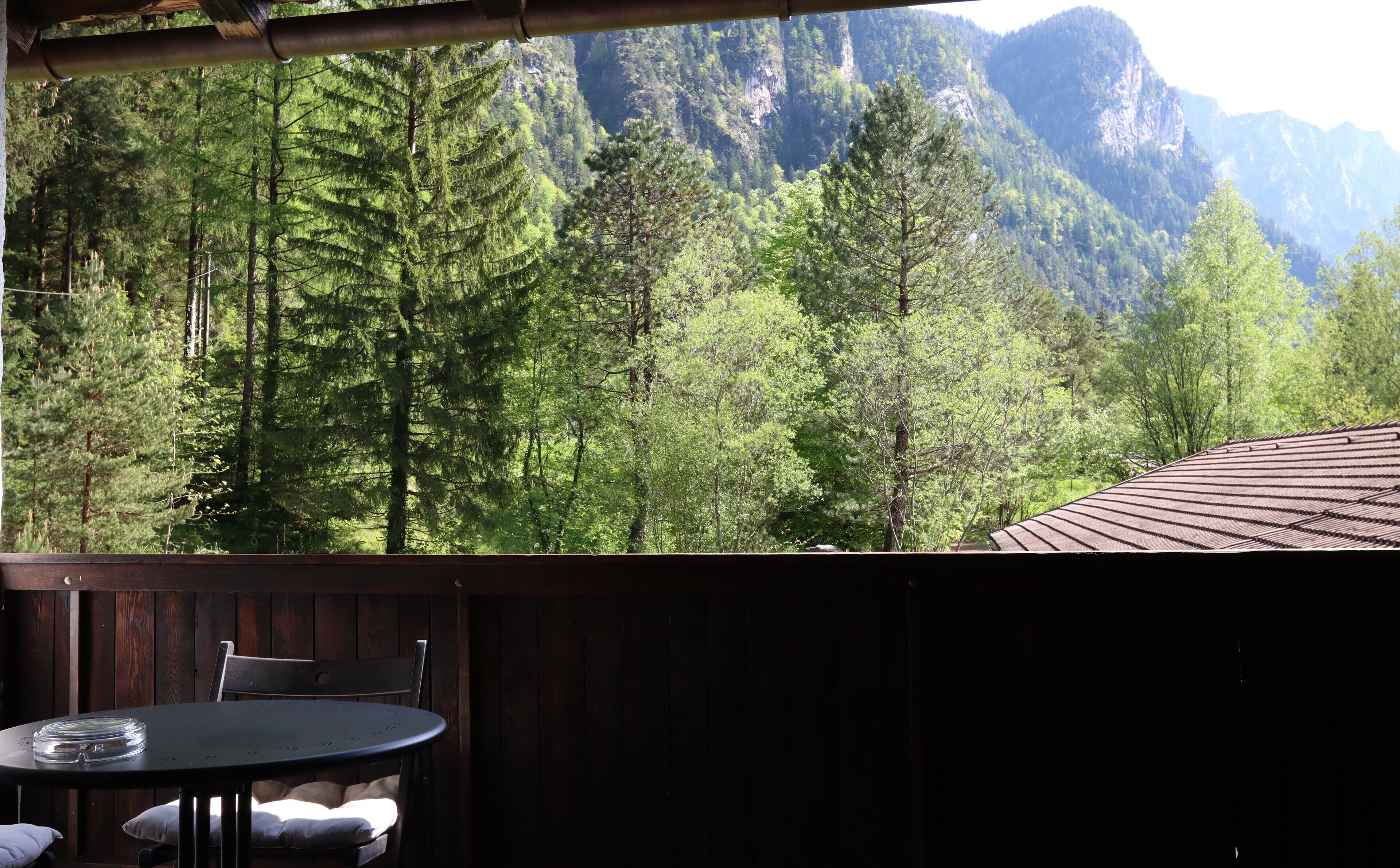 Eine Holzterrasse mit Tisch und Stühlen mit Blick auf eine bewaldete Berglandschaft.