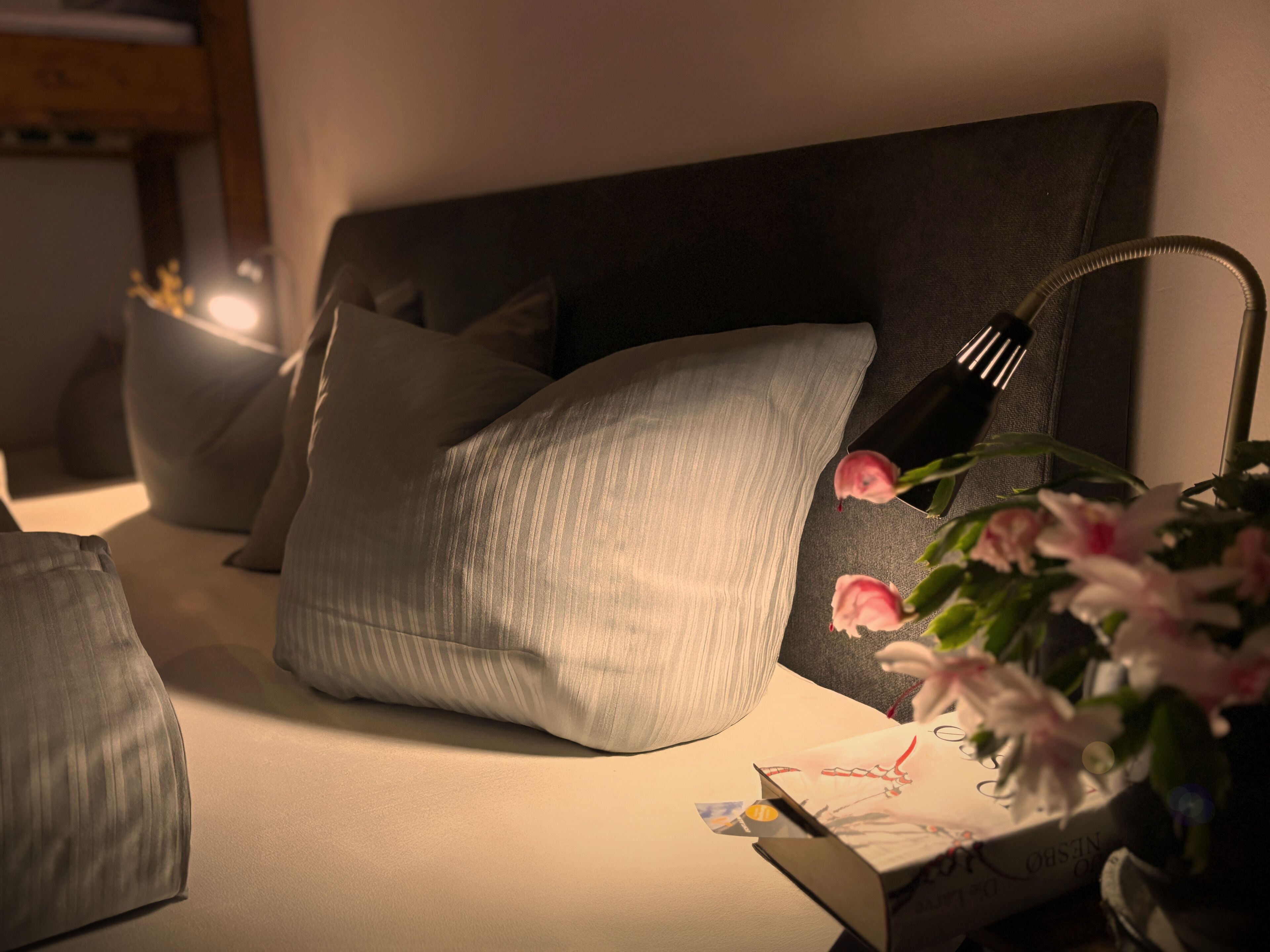 Un lit bien fait, avec des oreillers, une lampe de chevet et un vase rempli de fleurs.