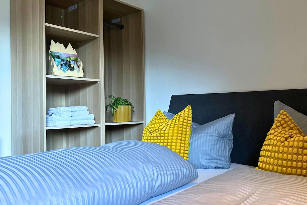 A bedroom with a bed, a wardrobe, and a shelf with folded towels and a decorative item.