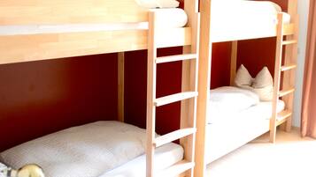 Ein Stockbett mit Holzlade, ein kleiner Nachttisch mit Pflanze und eine rote Wand.
